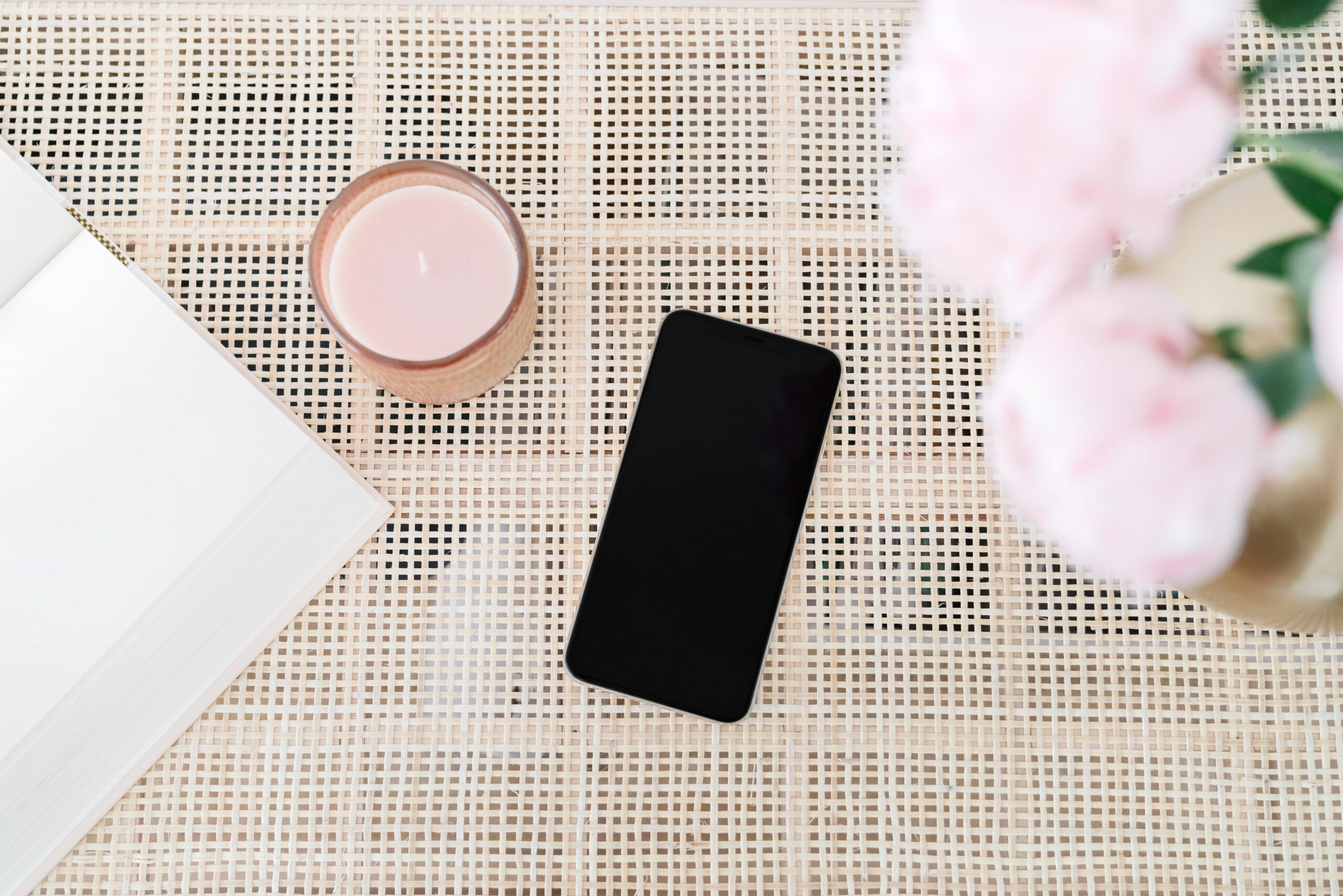 an iphone laying on a table with a candle and pink flowers