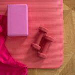 pink sports equipment including a yoga mat, a pair of dumbbells, a yoga block, and a towel
