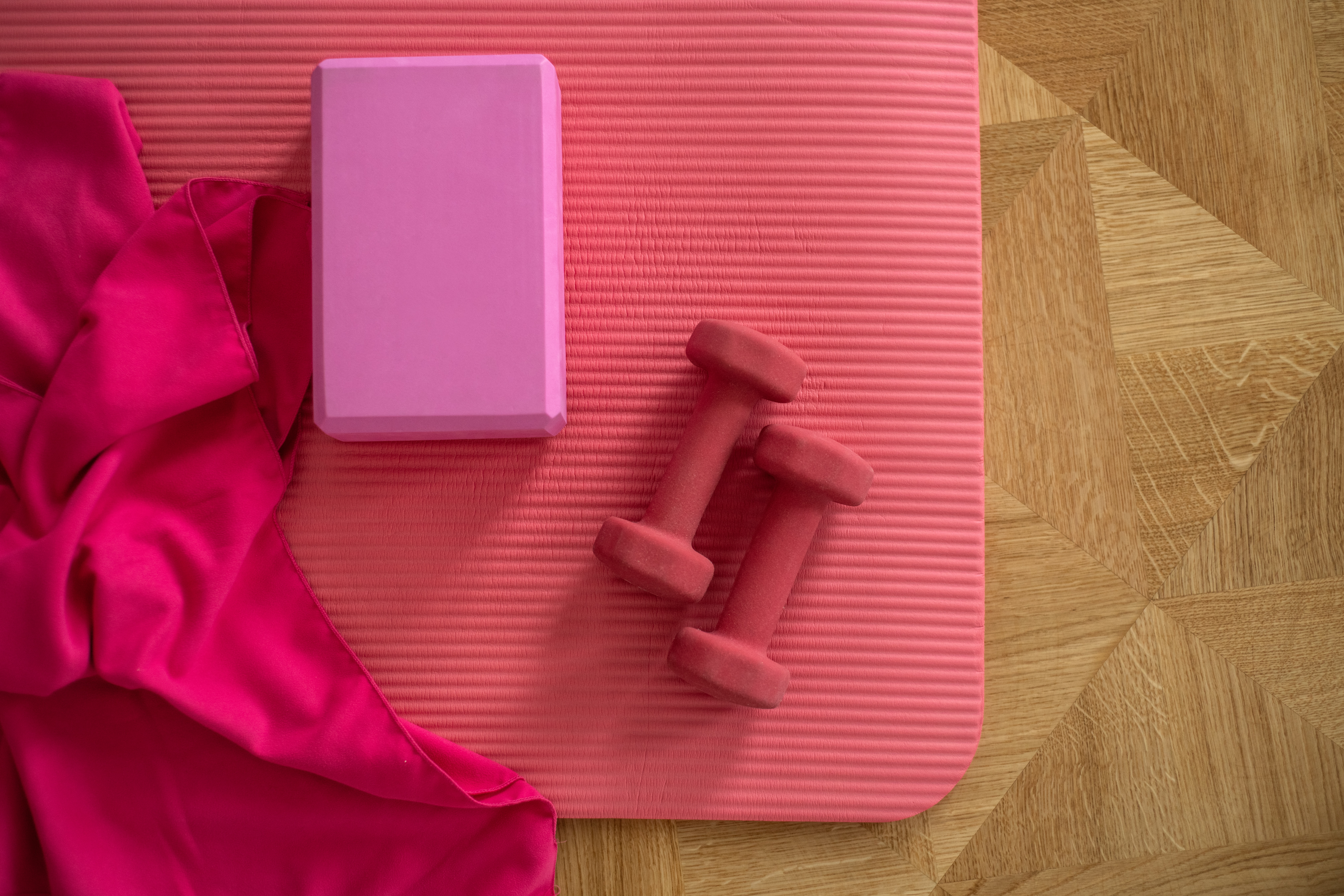 pink sports equipment including a yoga mat, a pair of dumbbells, a yoga block, and a towel
